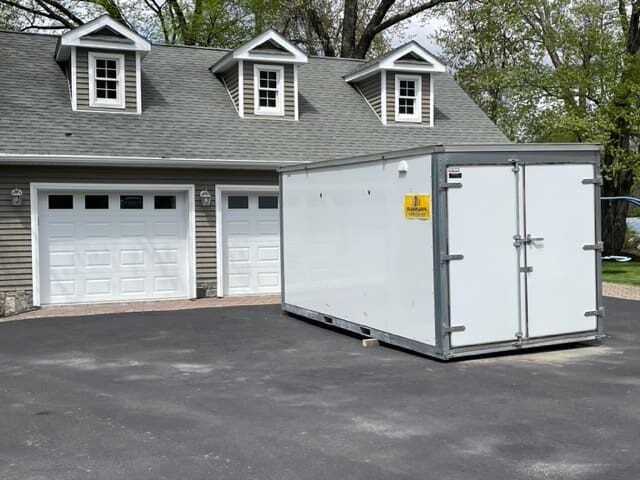 A white storage container sitting in front of a garage.